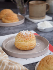 Close up of French cream puff crack bun (Choux au Craquelin) in a plate, topped with grated coconut filling with cup of coffee in background. It's a dessert base of savory choux dough bun 