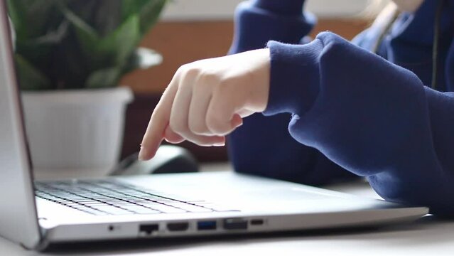 A child's hand in a blue jumper presses the button of the laptop keyboard twice with his index finger. Children on the Internet, information security. Close-up.