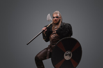 Fototapeta na wymiar Studio shot of fearful nordic barbarian with axe with shield dressed in black fur.