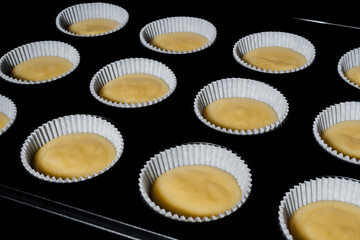 Twelve uncooked yellow cupcakes, muffins in muffin tin in electric oven - close up. Homemade bakery, food, cooking and pastry concept