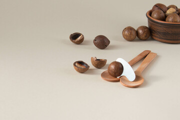 Macadamia nuts in ceramic bowl on beige background. Nuts with sawn nutshells and with opener key on the wooden spoon. Healthy snack, superfood.