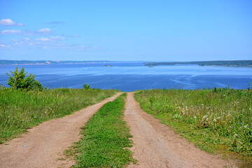 A dirt country road leads to the sea on horizon with blue sky