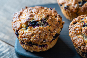 Delicious muffins with blueberries on a wooden table, closeup. Sweet pastries on the board. Fresh cupcakes for breakfast