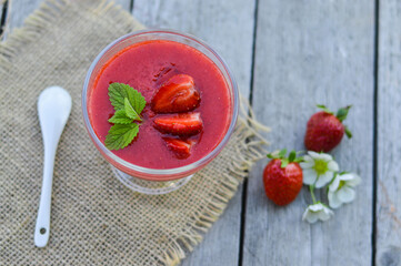 Strawberry smoothie in a glass decorated with mint leaves on rustic background, fresh fruit juice is red, detox food, diet and healthy breakfast, top view