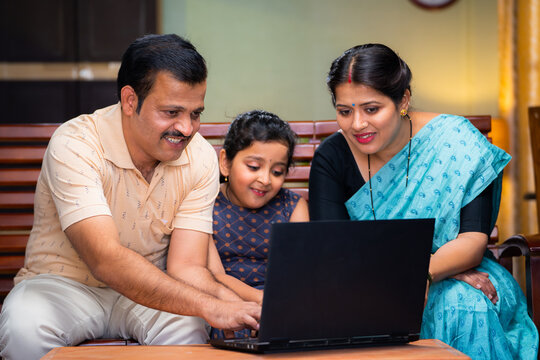 Happy smiling couple with daughter watching laptop while sitting on sofa at home - concept of technology, weekend holidays and relaxation
