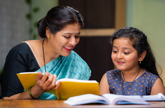 Mother teaching his daughter for reading book at home - concept of education, home tutor and parenthood