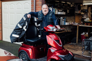 Portrait of elderly man standing near mobility scooter on the background of his garage. Modern...