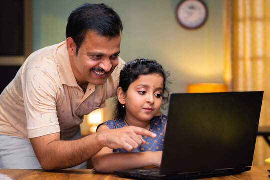 Father teaching or explaining from laptop to kid at home - concept of home schooling, caring and childhood growth or development.