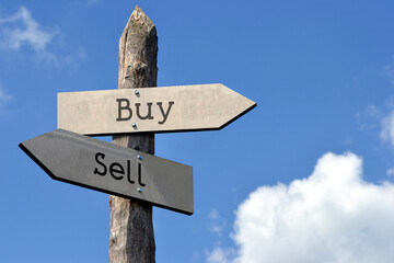 Buy or sell - wooden signpost with two arrows, sky with clouds