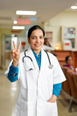 Indian female doctor showing victory sign at hospital.