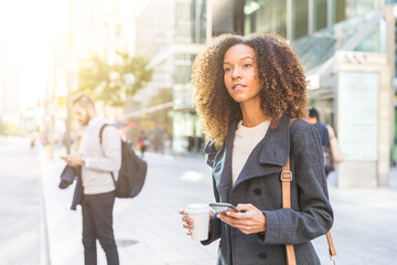 Business woman holding a mobile phone and waiting by the street in the city