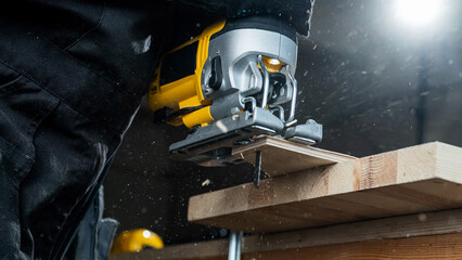 Close-up of a man cutting a wooden plank with an electric jigsaw in a workshop.