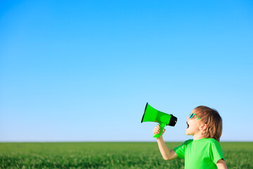 Happy child shouting through loudspeaker against blue summer sky - 580753053