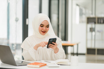 Muslim business lady wearing hijab and using smartphone in office.