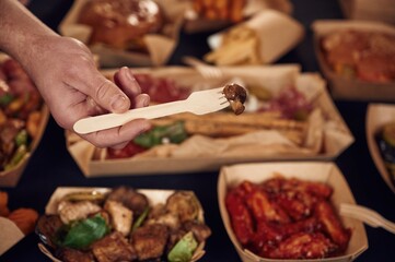 Man is holding fork with mushroom. Close up view of table with food on it. Meat, vegetables