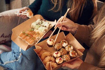 Two women are sitting and eating sushi indoors together