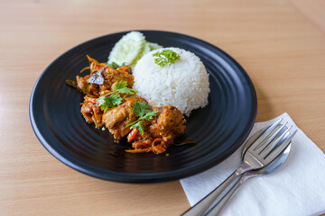 Thai Fusion food style : Homemade Rice with Stir-fried chicken with tom yum seasoning is in a black dish and placed on a wooden table.