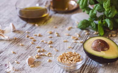 Basil, pine nuts, garlic, olive oil, parmesan and avocado on a kitchen table.  Ingredients  for...
