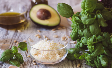 Basil, pine nuts, garlic, olive oil, parmesan and avocado on a kitchen table.  Ingredients  for Pesto recipe