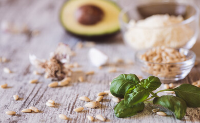 Basil, pine nuts, garlic, olive oil, parmesan and avocado on a kitchen table.  Ingredients  for...