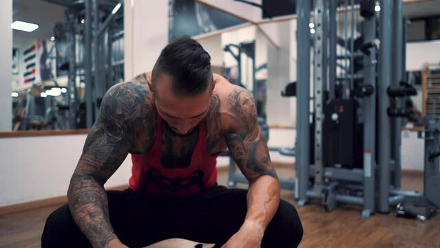 Young and handsome tattooed man training hard in gym. Lifting weights.