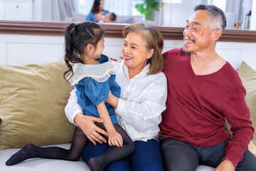 Happy grandparent older adult granny relax sitting on sofa embracing preschool child granddaughter