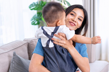 Fototapeta premium Mum holding embracing cute small infant boy son cuddling and playing sweet moment together at home