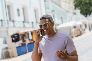 Overjoyed african american man in sunglasses talking on mobile phone on urban street. - Powered by Adobe