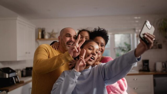 Teen girl taking selfie on phone with family in kitchen