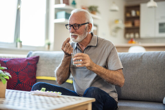 Senior man takes pill with glass of water in hand. Stressed mature man drinking sedated antidepressant meds. Man feels depressed, taking drugs.