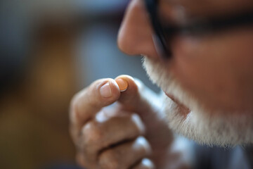 Senior man takes pill with glass of water in hand. Stressed mature man drinking sedated antidepressant meds. Man feels depressed, taking drugs.