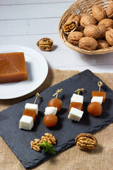 Fresh goat cheese and quince jelly skewers with walnuts on a black slate plate.