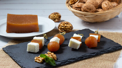 Fresh goat cheese and quince jelly skewers with walnuts on a black slate plate.