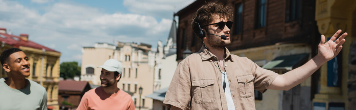 tour guide in sunglasses and headset pointing with hand during excursion on Andrews descent in Kyiv, banner.