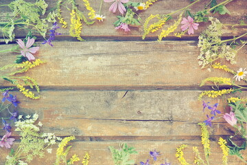 Multicolored wildflowers are arranged in a circle on a wooden table background. Chamomile, sweet clover, wild geranium, bluebells, parsley inflorescences. Horizontal boards. Romantic Provence style
