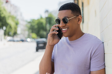 Cheerful african american man in sunglasses talking on smartphone on blurred urban street.