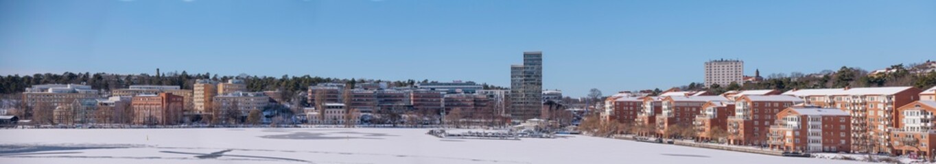 Fototapeta na wymiar The bay Alviks Strand with waterfront apartment an office buildings, a snowy sunny spring day in Stockholm