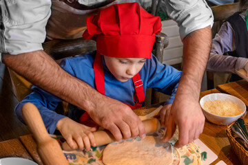 The cook teaches a boy in a cook's costume to cook pizza. Master class. Men's hands close-up.