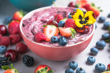 Two summer acai smoothie bowls with strawberries, blueberries,   on gray concrete background. Breakfast bowl with fruit and cereal, close-up, top view, healthy food