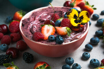 Two summer acai smoothie bowls with strawberries, blueberries,   on gray concrete background. Breakfast bowl with fruit and cereal, close-up, top view, healthy food
