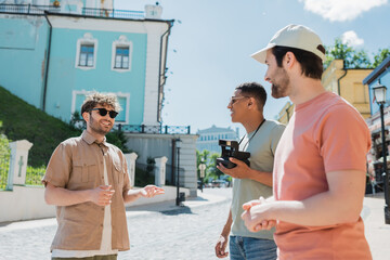 cheerful tour guide gesturing during excursion with multiethnic travelers on Andrews descent in...