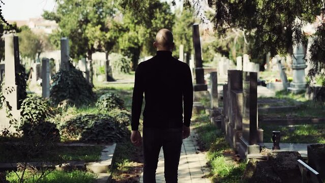 Young sad and serious man in black at the cemetery paying respect at grave and visiting relative commemorating ancestors
