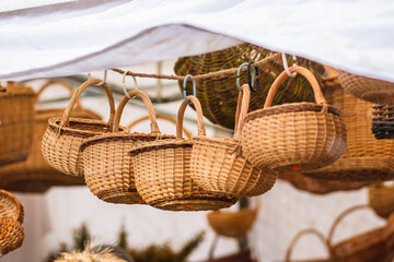 Group of hanging empty wicker baskets in a tent or stall for sale in a street market or traditional fair in winter or spring under the snow - obrazy, fototapety, plakaty