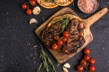Steaks. Sliced grilled meat steak New York or Ribeye with spices rosemary and pepper on black  board. Top view.