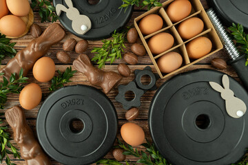 Gym dumbbells barbell weight plates, chocolate Easter bunnies, eggs and boxwood branches. Healthy diet choice concept. Fitness workout, sport training flat lay composition.