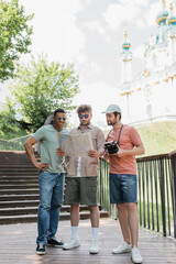 Obraz premium interracial travelers with city map standing on stairs near St Andrews church on blurred background in Kyiv.
