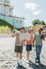 full length of multiethnic tourists walking with tour guide holding travel map and pointing with...