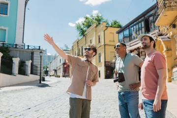 Fotobehang Kiev tour guide in sunglasses pointing with hand during excursion with interracial tourists on Andrews descent in Kyiv.
