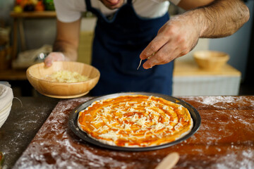 Professional Italian chef baking a cheesy Hawaiian pizza at home. Italian chef topping a Hawaiian pizza with mozzarella cheese, tomato sauce, vegetable, and meat before bake in the oven.