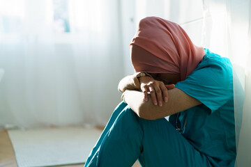 Unhappy - tired Muslim female surgeon doctor sitting on the floor in the hospital. Overworking...
